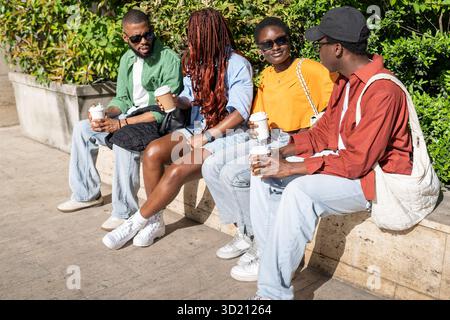 Happy African American students sitting on park bench, joking chatting over coffee after exams Stock Photo