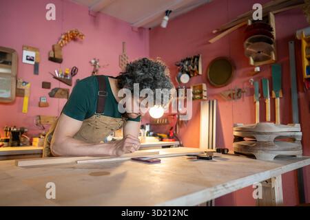 Focused woodworker carefully reviews client order specifications using smartphone in workshop Stock Photo