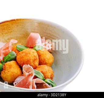 Crispy cheese balls garnished with prosciutto and fresh herbs in elegant bowl setting Stock Photo
