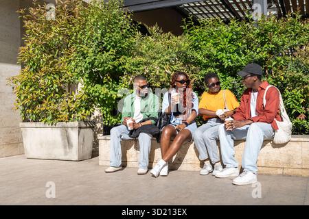 Group of cheerful African American student friends sharing stories with coffee, hanging out in park Stock Photo
