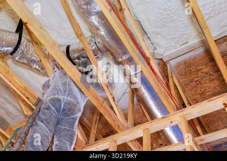 Construction worker is busy installing ductwork inside new home under construction, working on ceiling supports. Stock Photo