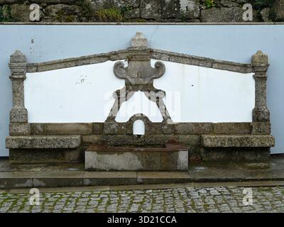 Old stone fountain with white wall and cobblestone floor Stock Photo
