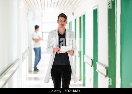 Doctor Reading Documents in Hospital.Young male doctor walking in hospital hallway while reading patient documentation. Clinical Stock Photo