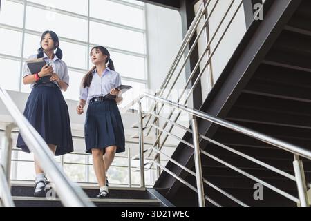 Smart students women teen in uniform standing together at modern school campus indoor. Thai high school student female. Stock Photo