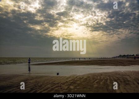 Sun Rays Over Quiet Beach With People By Shoreline and Distant Pier at Dusk Calm Stock Photo