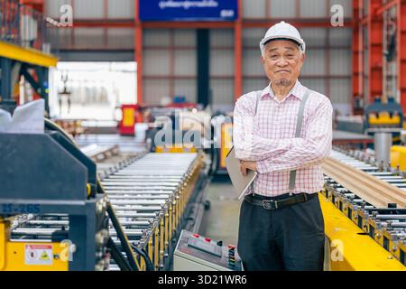 Senior Asian engineer leader man, technician worker happy smiling, confident professional with heavy industry factory machine and safety hardhat Stock Photo
