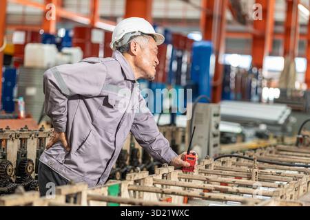 Senior Asian worker muscle pain, Suffer from back pain, health problem at work, hard work in heavy industry factory. Stock Photo