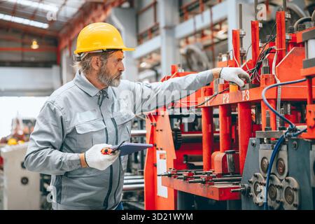 Professional senior Industrial worker in protective helmet and uniform service machinery in factory, expert engineer technician maintenance heavy mach Stock Photo