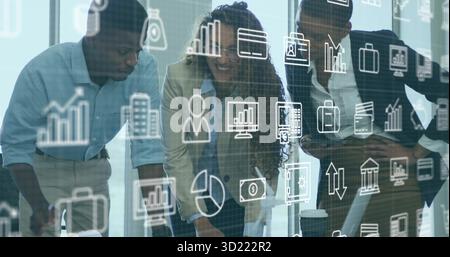 Leaning three-person team reviewing laptop and documents in glass-walled room, with analytics icons Stock Photo