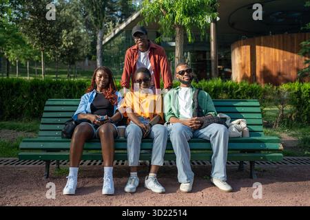 Happy young couples, black men and women, sit on park bench during double date, looking at camera Stock Photo