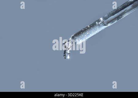 Close-up of transparent liquid drop from glass pipette against light blue Stock Photo