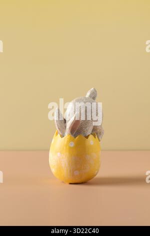 A white rabbit hid in an Easter egg on a yellow background. Festive Easter card. Stock Photo