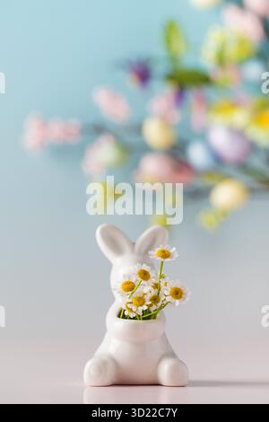 Easter white hare with a bouquet of daisies on a blue floral background. The concept of spring and Easter. Stock Photo