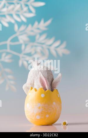 A white rabbit hid in an Easter egg on a blue background. Festive Easter card. Stock Photo