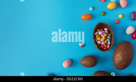 Chocolate Easter egg with colorful dragees inside on a blue. Happy Easter. Copy space Stock Photo