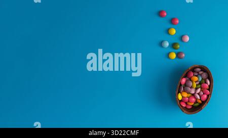 Chocolate Easter egg with colorful dragees inside on a blue. Happy Easter. Copy space Stock Photo