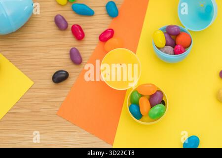 Bright background with candies in the form of Easter eggs in plastic eggs. Egg hunt concept. Happy Easter. Top view. Stock Photo