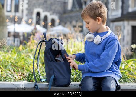 Smiling boy student with wireless earphones opens schoolbag Stock Photo