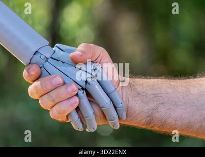 Robot and human hands. Robot and male hand handshake on green nature. Ai and human hands making handshake. Robotic hands interacting with human hand Stock Photo