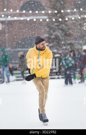 Joyful middle aged man in yellow jacket, beige trousers on ice rink, outdoors in snowy winter day Stock Photo