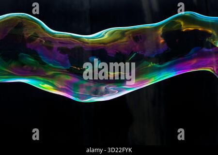 A dazzling and floating soap bubble hose in the colors of the rainbow against black background, Recklinghausen, Germany, Europe Stock Photo