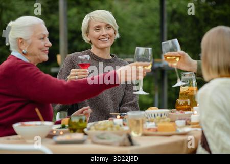 Caucasian Senior Woman and Middle Aged Women Toasting during Outdoor Dinner Gathering Stock Photo