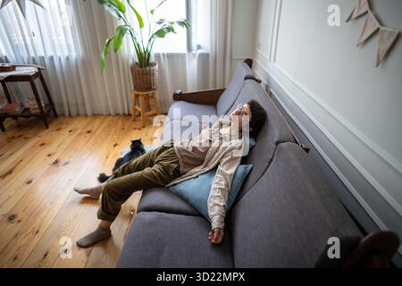 Tired lazy woman lying on sofa and looking up, bored and apathetic female and cat in isolation Stock Photo