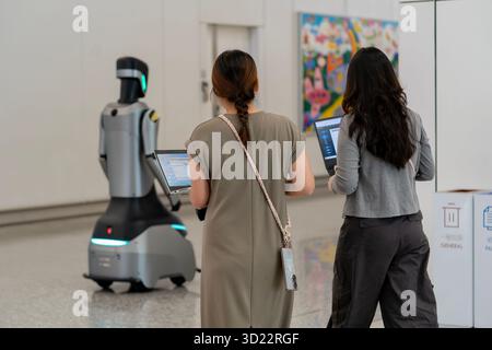 Hong Kong, China - September 20, 2025: Two women working on laptops with a service robot on the departure level of Hong Kong International Airport. Stock Photo