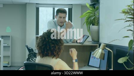 Pointing man guiding woman in wheelchair on tablet at office counter, with chart on laptop Stock Photo