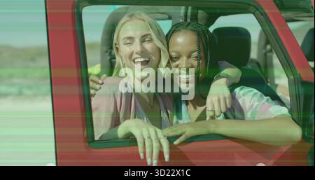Laughing two friends hugging, leaning out of red car window at sandy roadside dunes, with rings Stock Photo