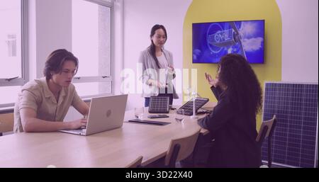 Collaborating business team designing power in boardroom, with solar panels and wind turbine models Stock Photo