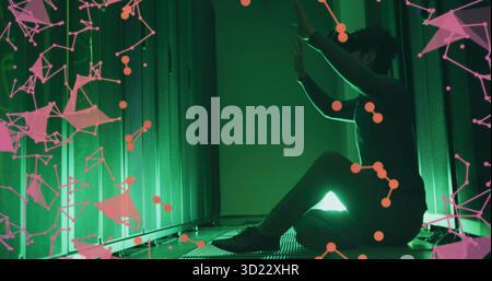Kneeling technician in dark outfit touching server rack in datacenter green lighting, pink overlay Stock Photo