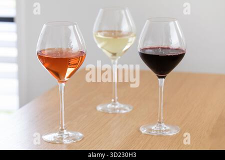 Three glasses of wine. Roses, white and red, stand on a wooden table Stock Photo