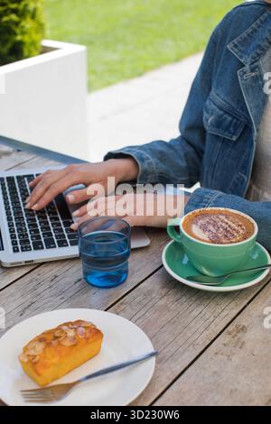 Woman with coffee cup typing on laptop sitting at cafe table Stock Photo