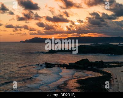 Stunning sunset over a rocky coastline with silhouettes and dramatic clouds. Lombok, Gerupuk, Indonesia Stock Photo