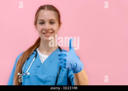 Young caucasian woman doctor in a blue uniform on an isolated pink background gives a thumbs up Stock Photo