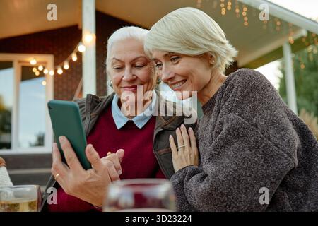 Senior Caucasian Woman and Middle Aged Caucasian Woman Smiling While Using Smartphone Stock Photo
