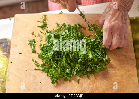 Elderly caucasian hands chopping fresh parsley on wooden cutting board Stock Photo