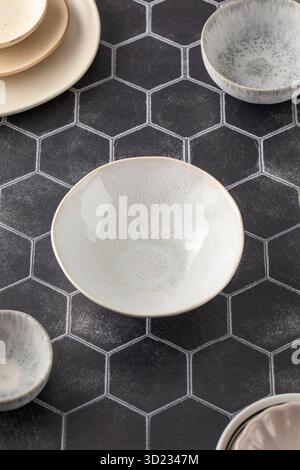 Elegant assortment of ceramic dishes on a chic dark hexagonal tile surface. Kitchen, menu. Stock Photo