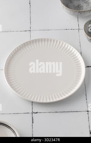 Minimalist white ceramic plate on a tiled surface. Kitchen, menu. Stock Photo