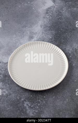 Elegant white plate on textured grey backdrop, ideal for showcasing culinary designs with a touch of sophistication. Stock Photo