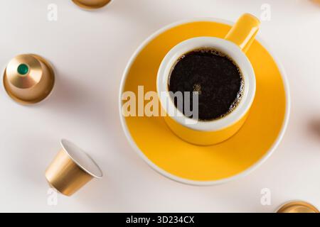 Yellow coffee cup with golden coffee capsules on a white background. Stock Photo