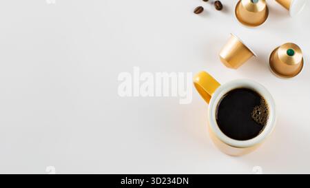 Yellow coffee cup with golden coffee capsules and beans on a white background. Copy space Stock Photo