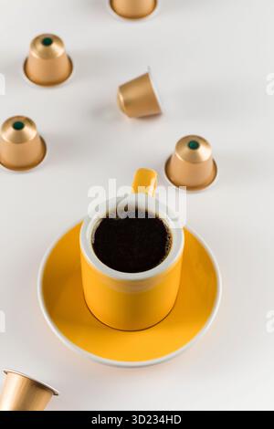 Yellow coffee cup with golden coffee capsules on a white background. Stock Photo
