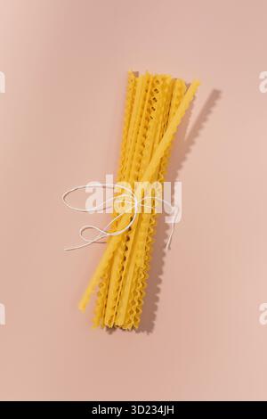 Bundle of uncooked Curly Fettuccine tied with string on a pink background Stock Photo