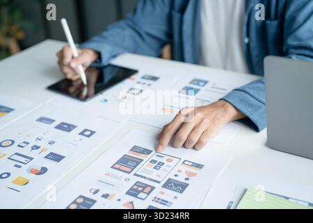 UX UI Designer Planning innovative Mobile App with Paper Wireframe Designs at Workspace. Stock Photo