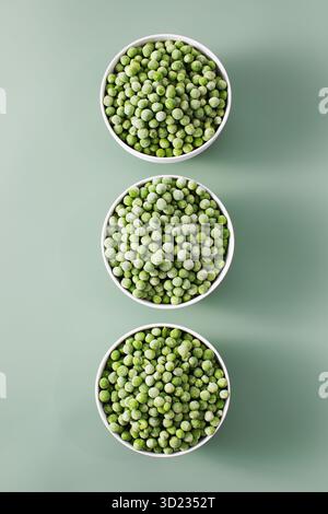 Three white bowls filled with frozen green peas on green background. Stock Photo