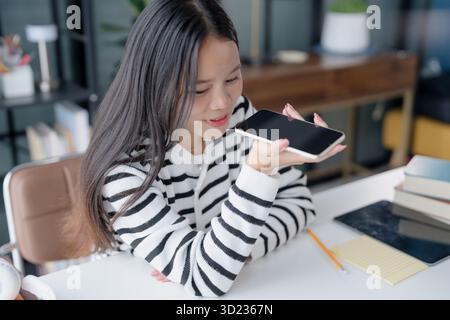 Asian Woman Engaging with Voice Assistant on Smartphone in Modern Home Stock Photo