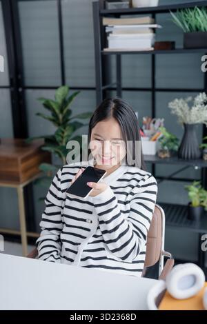 Asian Woman Engaging with Voice Assistant on Smartphone in Modern Home Stock Photo