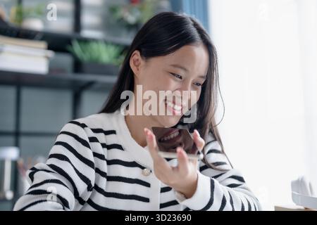 Asian Woman Engaging with Voice Assistant on Smartphone in Modern Home Stock Photo